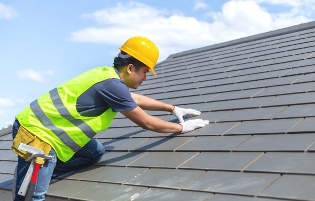 Builder Working On Roof Of New Building, Construction worker wearing safety harness and safety line working on roof new warehouse.